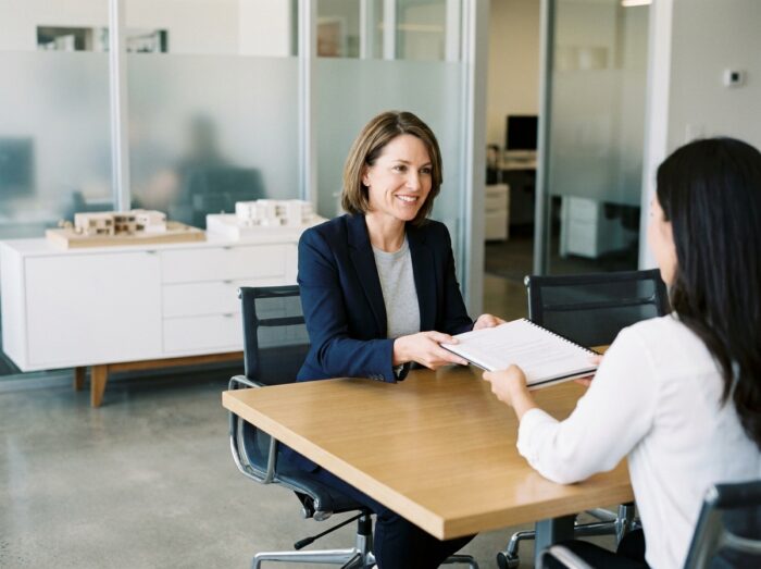 Professionnelle en architecture d'intérieur remettant son CV et portfolio à un recruteur lors d'un entretien en agence